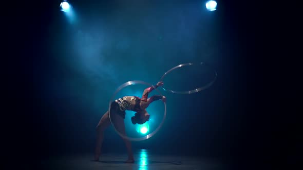 Acrobat Performs with Hoops. Blue Smoke Background. Slow Motion