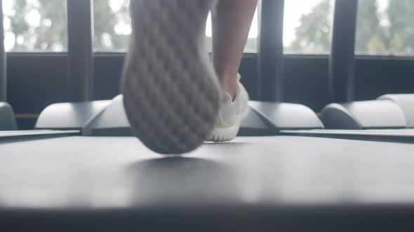 Young Asian guy feet in sneakers exercise running on treadmill fat burning workout in fitness class.