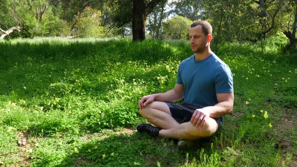 A man sitting in a meditation pose in a green sunny forest practicing deep breathing exercises to re