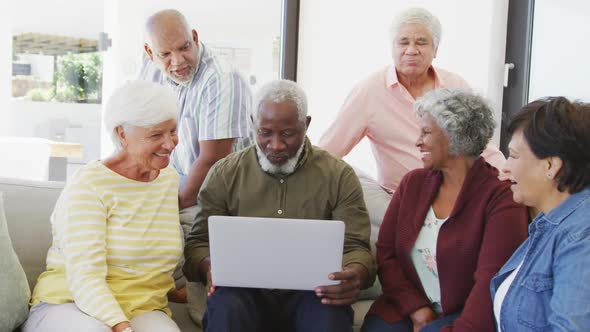 Happy senior diverse people talking and using laptop at retirement home