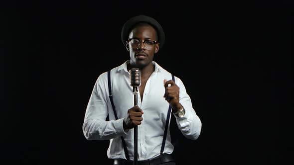 African American in a Studio Is Singing Songs Into a Microphone. Black Background