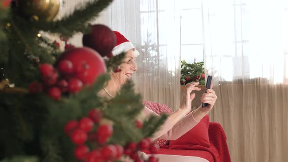 Pensioner in Santa Hat Holds Smartphone and Waves Hand