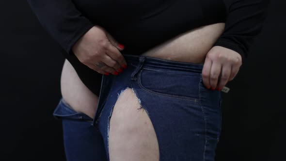 Fat Woman with Cellulite Trying to Put on Jeans on Black Background