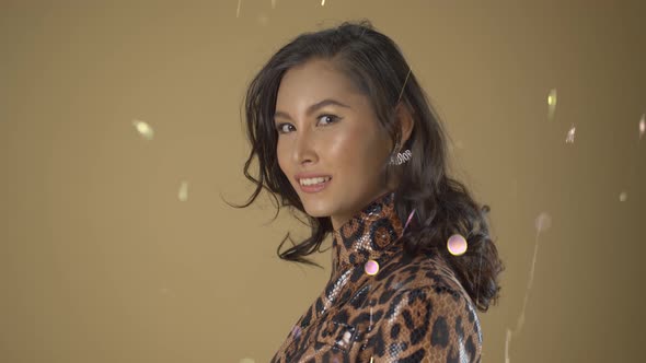 Asian modle poses for headshots with wind blowing her hair and sparkles and glitter in the wind on a