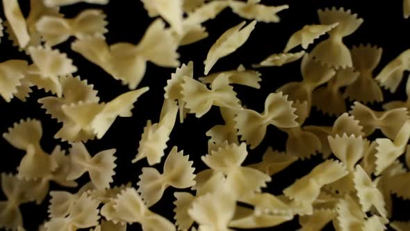 Farfalle Pasta Flies After Being Exploded. Pile of Italian Macaroni Bouncing Against Camera Black BG