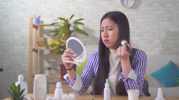 Portrait of a Disgruntled Asian Young Woman Using Makeup in the Living Room