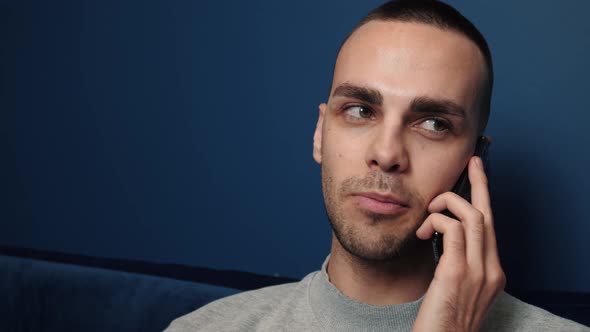 Handsome Caucasian Man Eating Snacks and Chatting on Cellphone While Watching TV at Home Couch