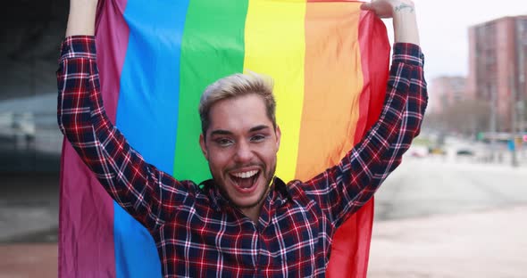 Gay man with makeup on having fun holding lgbt rainbow flag outdoor