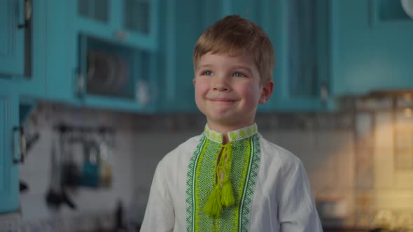 Blonde Boy in Embroidered National Clothes Smiling and Showing Emotions at Home on Blue Kitchen. Kid