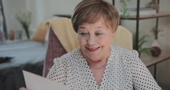 Close Up View of Smiling Woman Looking at Photo While Sitting on Chair at home.Elderly Lady in 70s