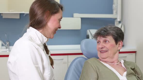 Beautiful female dentist laughing and talking with elderly female patient