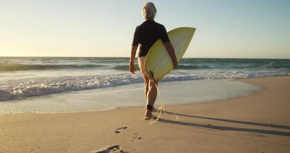 Senior man walking with surfboard at the beach