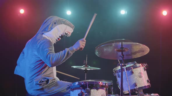 Side View of Musician in a Festive Shark Costume Plays Drums and Hits Percussion Cymbals