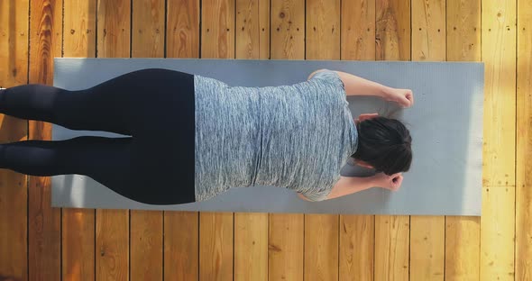 Woman in Tracksuit Stands in Plank Pose on Floor