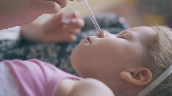 Mother Gives Nose Drops To Unhappy Girl on Soft Bed Closeup