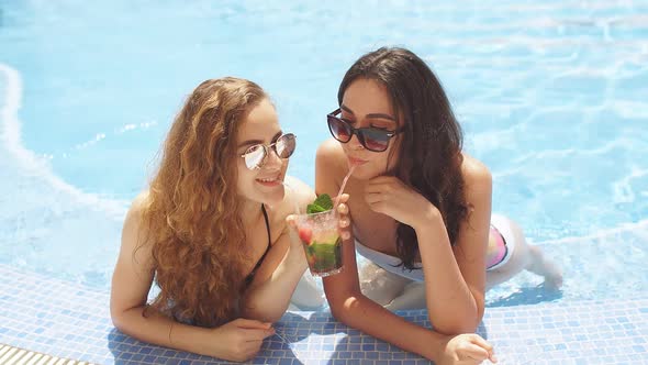 Two Young Girlfriends Sitting in Cool Swimming Pool in Resort Hotel on Vacation