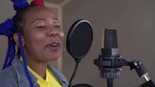 Young Black Woman Musician Singing Into a Microphone in a Recording Studio