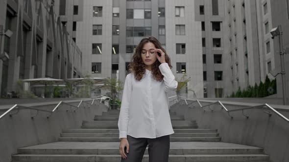 Young Girl Dressed In Business Style Clothes Stands On The Background Of Tall Building