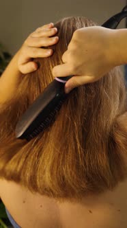 Rear view of the girl brushing her hair with a special electric straightening brush