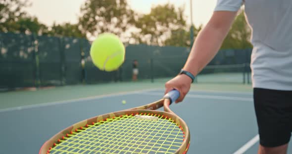 Male Arm Holds the Racket and Hits Small Yellow Ball