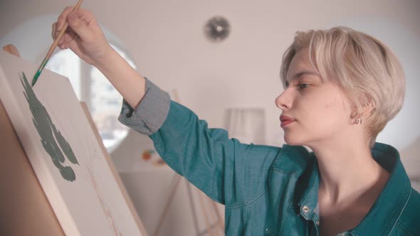 A Young Woman with Short Blonde Hair Painting with a Green Color in the Art Studio