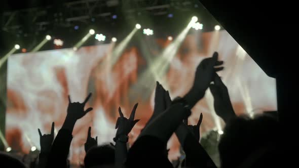 Audience with Hands Raised at a Music Festival and Lights Streaming Down From Above the Stage