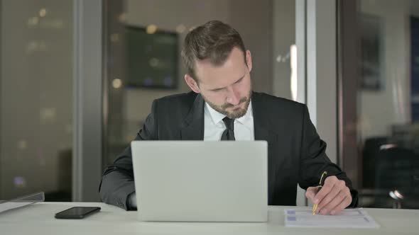 Young Businessman Working on Laptop and Document at Night