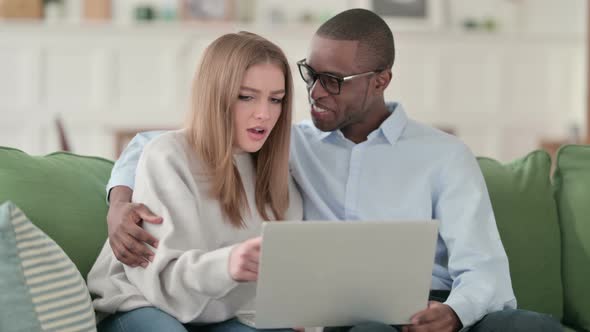Happy Mixed Race Couple Hugging While Using Laptop at Home