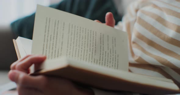 Closeup of Young Woman Reading Book in Cozy Living Room Turning Page Learning Studying Education