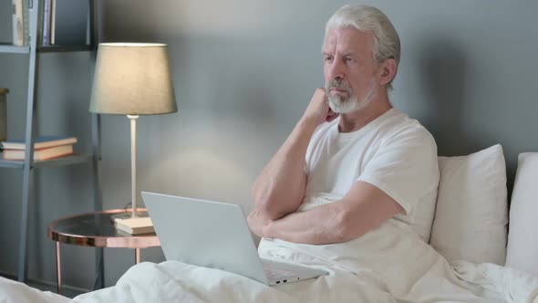 Old Man with Laptop Thinking in Bed