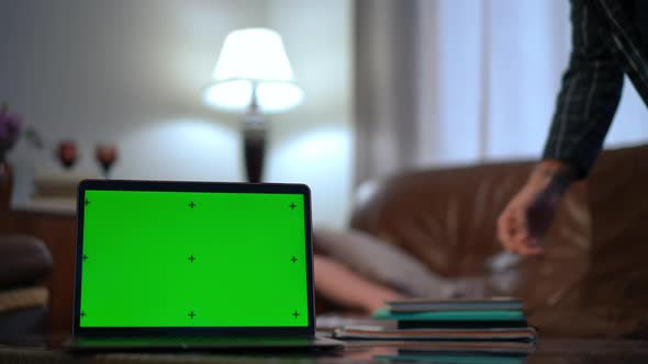 Chromakey Laptop in Living Room with Blurred Caucasian Man Entering with Books Sitting Down on Couch