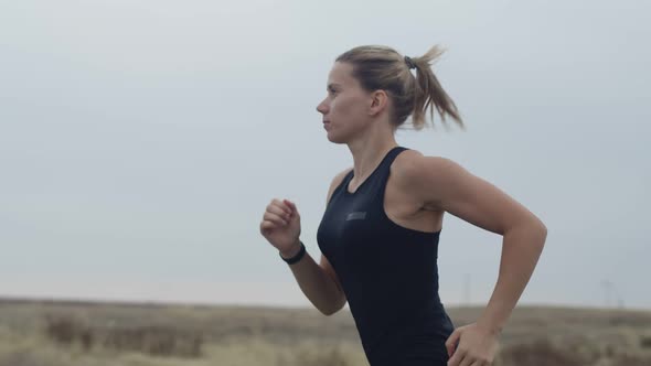 Sporty Caucasian Woman with Blonde Hair in Sportswear is Persistently Run Against the Background of