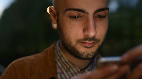 Portrait of young man gay using smart phone, face illuminated by screen light