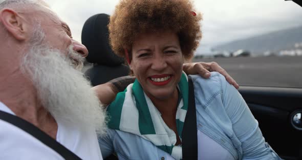 Multiracial senior couple having fun at summer vacation inside convertible car