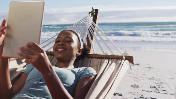 African american woman using digital tablet while lying on a hammock at the beach