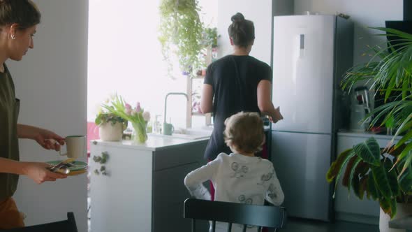 Lesbian Couple and Little Son Clearing Kitchen Table after Breakfast