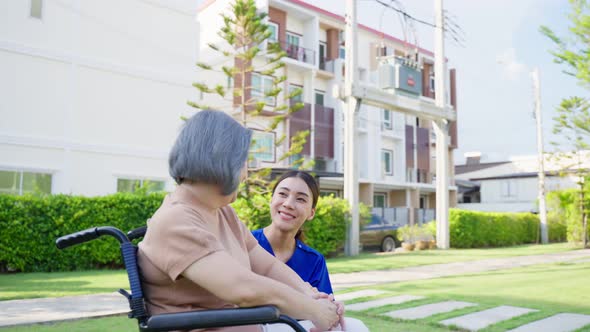 Asian caregiver nurse support old disabled woman on wheelchair outdoor.