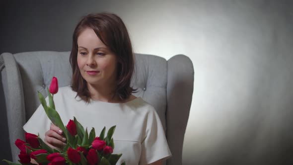 Beautiful Woman Smelling a Bouquet of Red Tulips on Chair