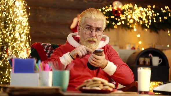 Santa Claus Watch Tv Holding Remote Control at Home. New Year Holiday. Santa Claus Relaxing After or