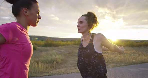 Two Multiethnic Girls Stretching Together in the Street Stretching Their Legs Before a Run