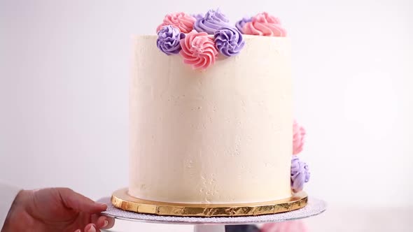 Time lapse. Flat lay. Piping pastel color buttercream rosettes on a white cake to make a unicorn cak