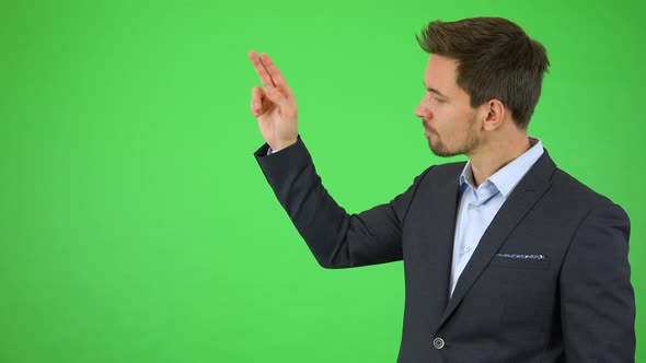 A Businessman Scrolls Through an Invisible List Next To Him and Smiles at the Camera - Green Screen