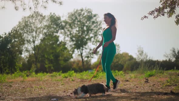 Beautiful athletic woman in a sporty turquoise overalls walks with her fluffy cat on a leash 
