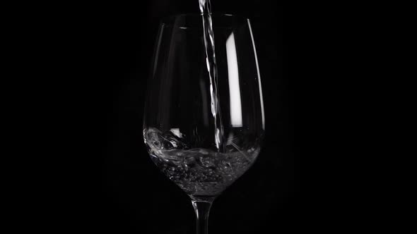 Close up slow motion shot of filling water in a red wine glas.