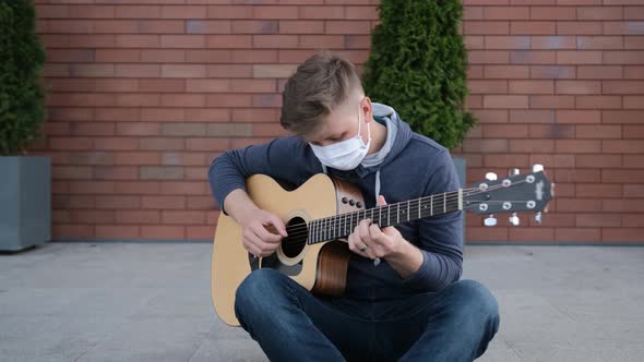 Artist Sitting on Sidewalk Is Playing at the Guitar