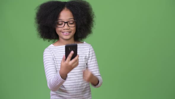 Young Cute African Girl with Afro Hair Using Phone and Celebrating