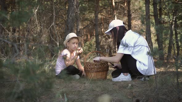 Mom and Little Daughter Go on the Road in the Autumn Forest. The Family Gather Mushrooms and Berries