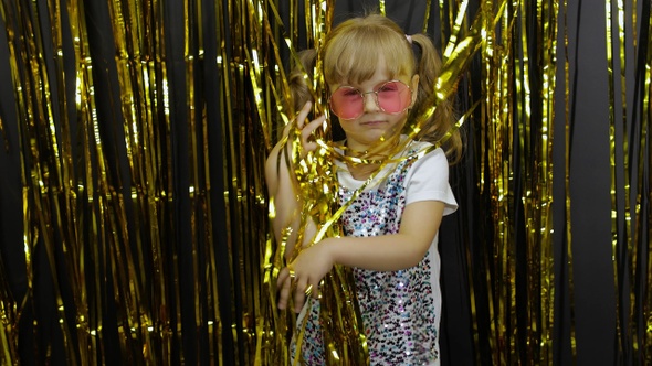 Happy Child Dancing, Playing, Fooling Around in Shiny Foil Fringe Golden Curtain. Little Blonde Girl