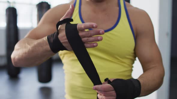 Mid section of caucasian male boxer wrapping boxing tape on his hands at the gym