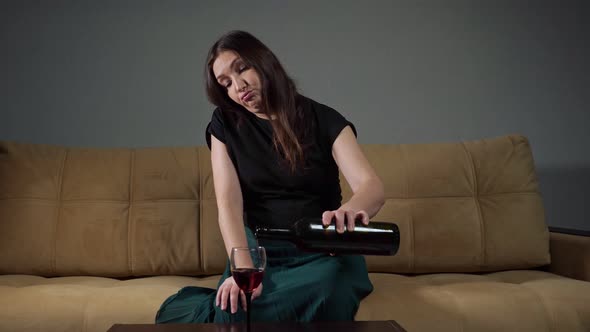 Tipsy Woman Pours Wine Into Glass Sitting on Soft Sofa